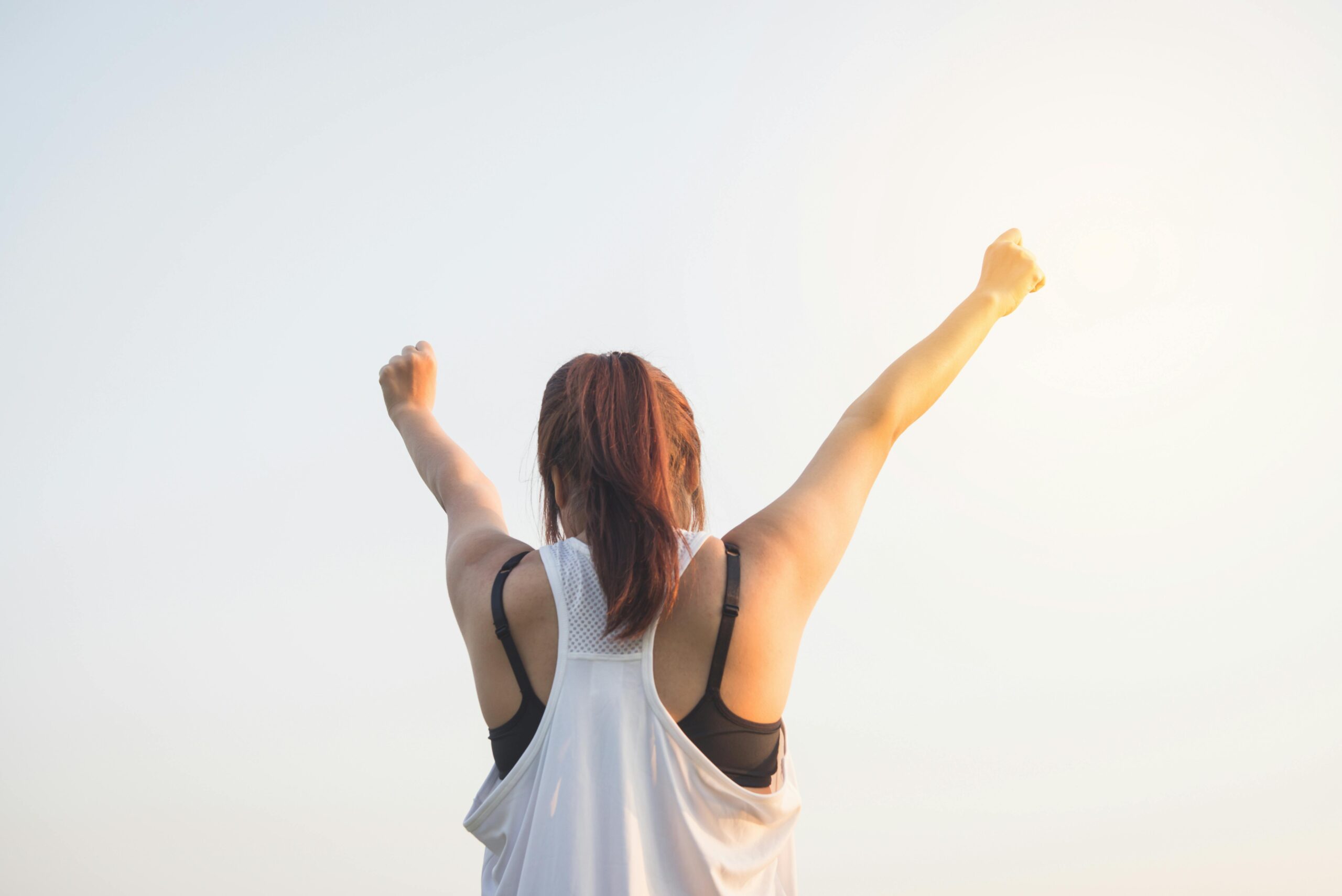 A woman with her arms stretched upwards in excitement against a clear sky.