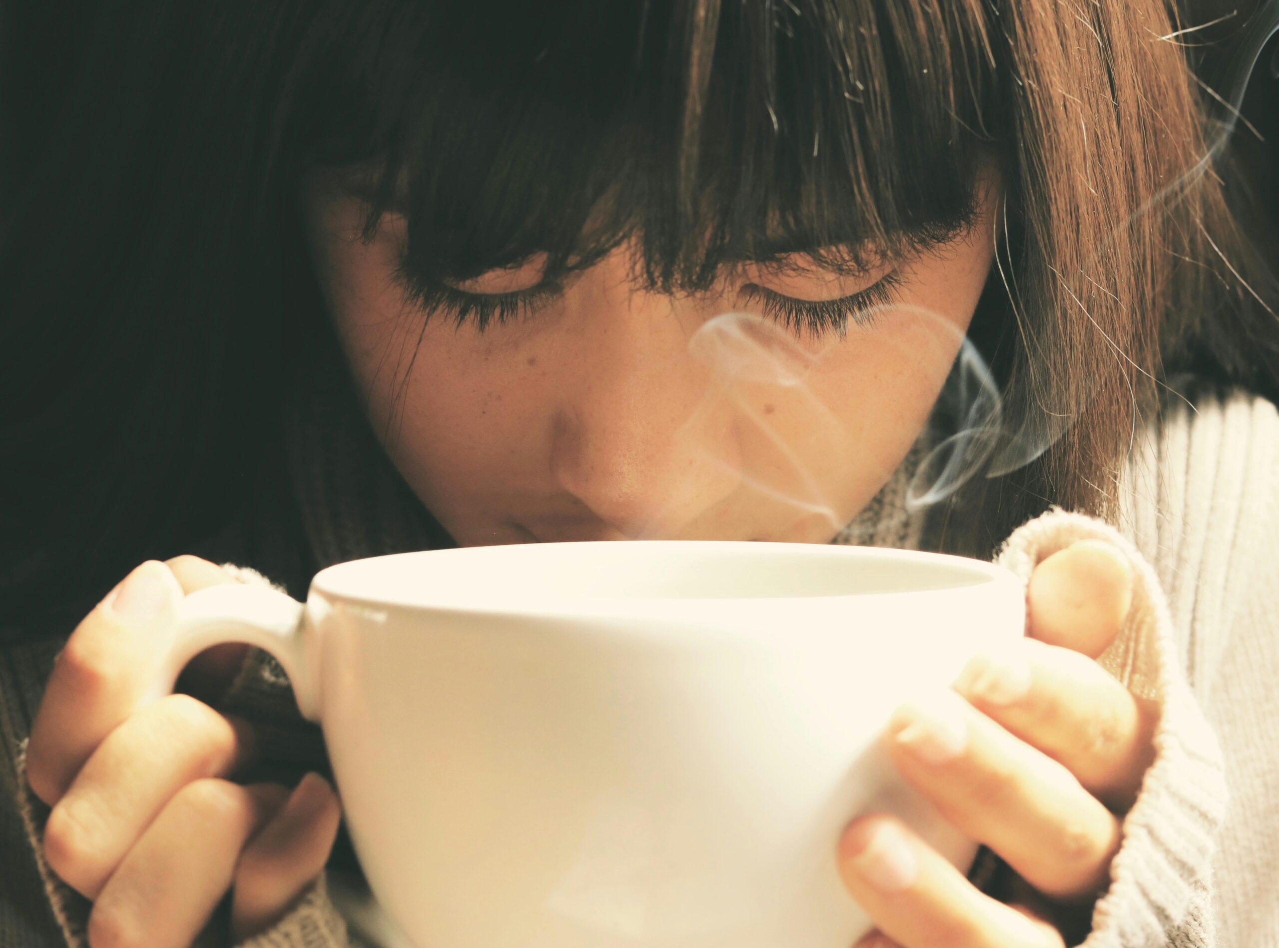 A woman holding a warm cup and smelling it.