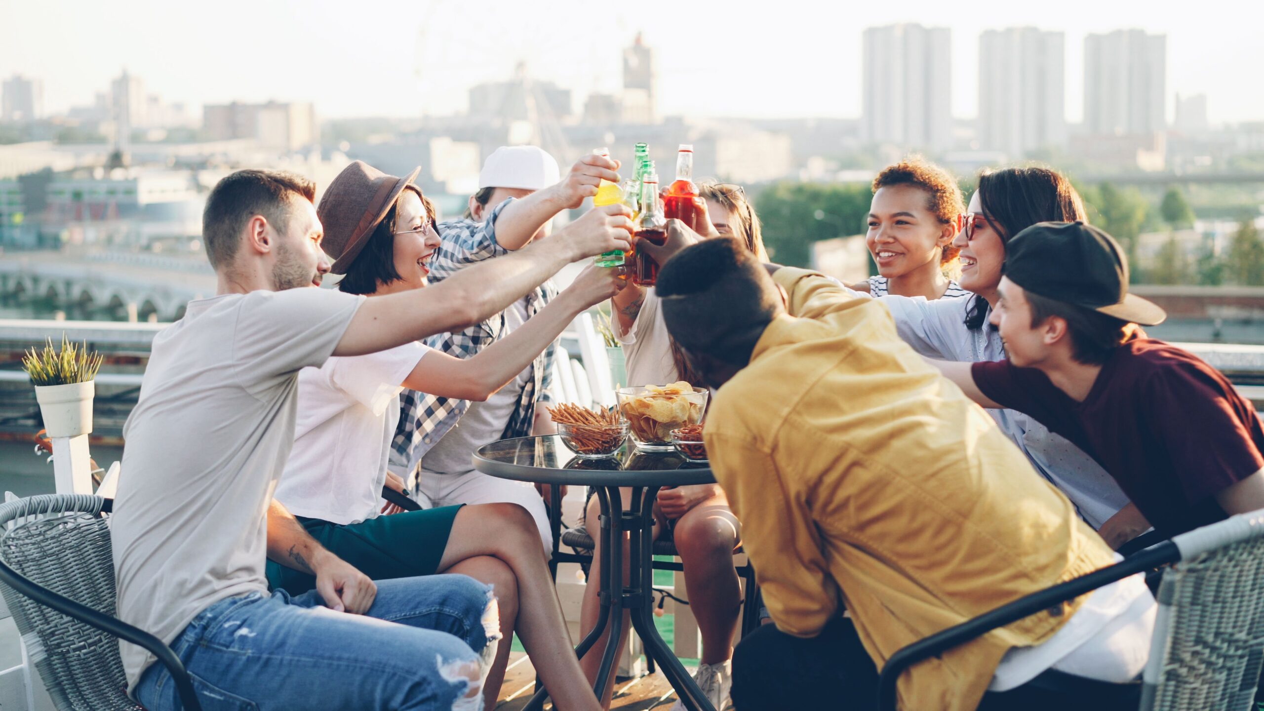 A large group of people are sitting around a table with snacks and holding up drinks.