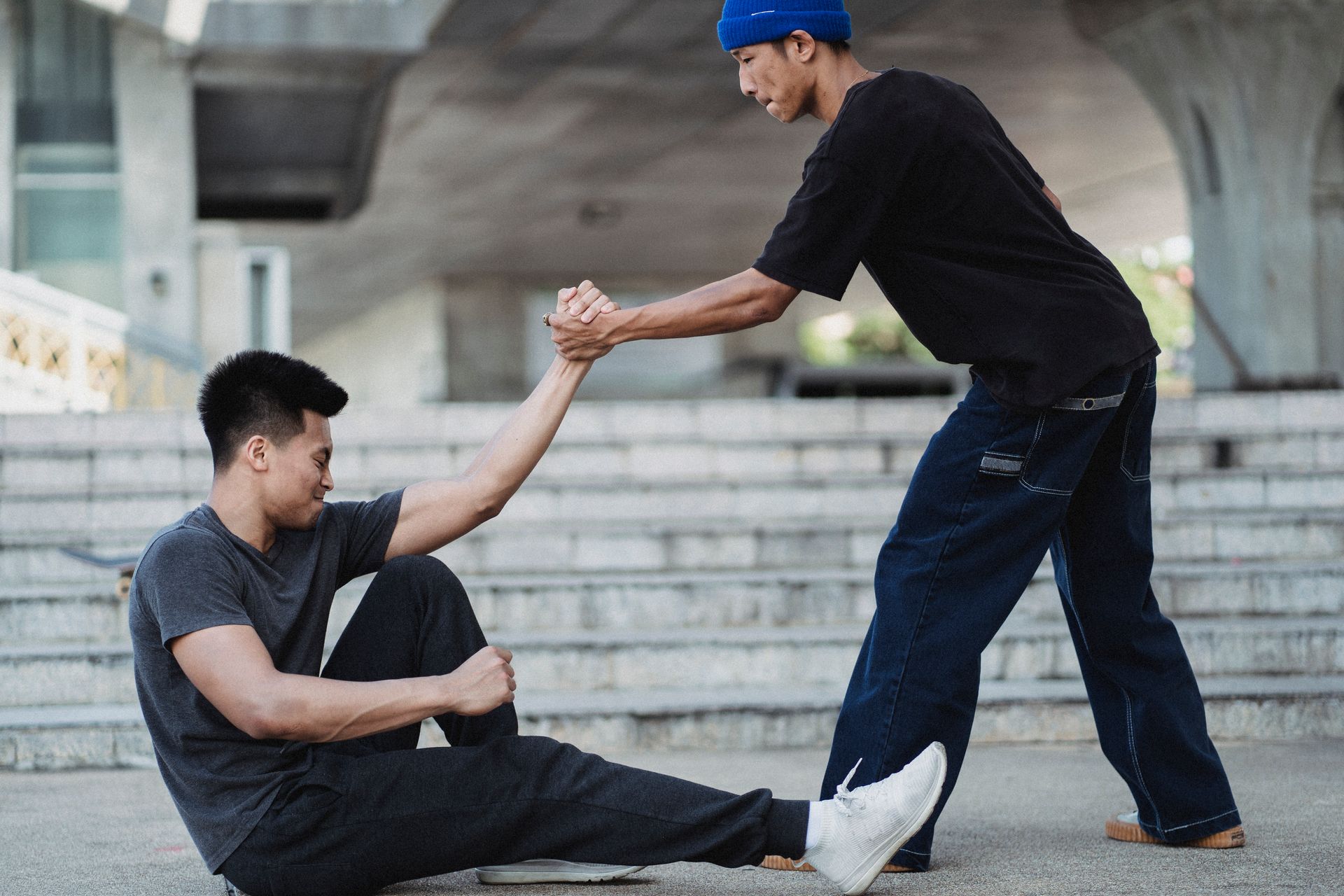 One man helping someone who is sitting down off the ground.